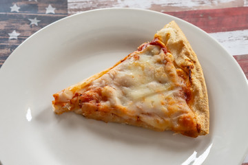 Slice of cheese pizza on white plate with USA flag background and room for text