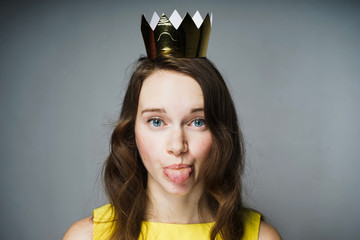 funny blue-eyed girl in a yellow dress shows a tongue, a golden crown on her head