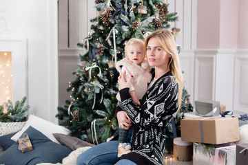 Cheerful mom embraces her cute baby daughter . Parent and little child having fun near Christmas tree indoors. Loving family Merry Christmas and Happy New Year