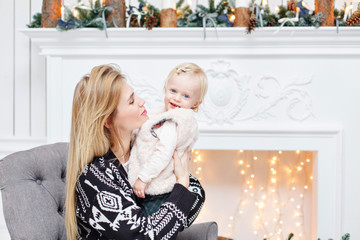 Cheerful mom embraces her cute baby daughter . Parent and little child having fun near Christmas tree indoors. Loving family Merry Christmas and Happy New Year