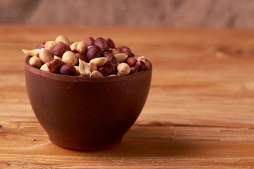 Deep fried peanuts in clay bowl over rustic wooden background. Selective focus