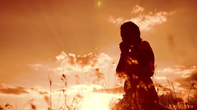 Girl folded her hands in prayer silhouette at sunset. woman praying on her knees. slow motion video. Girl folded her hands in prayer pray to God. the girl praying asks forgiveness for sins of