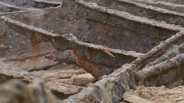 Zooming out from close up to a wide shot of a ship wreck's corroded remains on a beach in front of steep cliffs