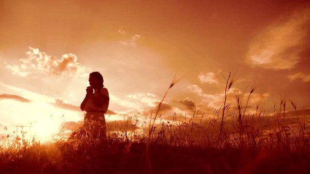 Girl folded her hands in prayer silhouette at lifestyle sunset. woman praying on her knees. slow motion video. Girl folded her hands in prayer pray to God. the girl praying asks forgiveness for sins