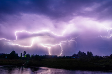 Composition photo of different lightning bolts. Thunderstorm with dramatic clouds. Lots of lightnings over the night village near river bank. Bad weather concept.