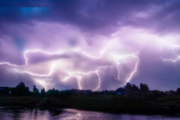 Composition photo of different lightning bolts. Thunderstorm with dramatic clouds. Lots of lightnings over the night village near river bank. Bad weather concept.