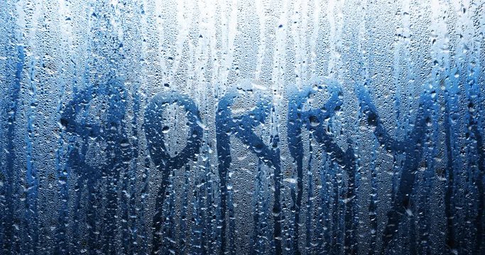 Handwritten sorry word on wet window with water drops.