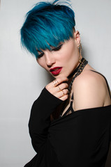 Fashion shot of a woman whith bright blue hair holding hugging herself on isolated gray wall background. Professional model posing for magazine cover