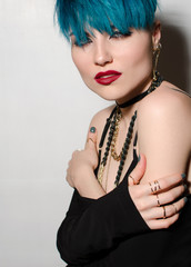 Fashion shot of a woman whith bright blue hair holding hugging herself on isolated gray wall background. Professional model posing for magazine cover