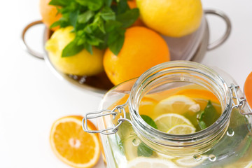 Healthy lemonade in mason jar with lemon, orange and mint on white table. Close up.