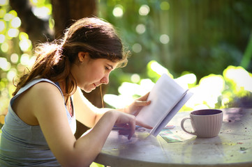 teenager student girl reading book with tea cup on summer garden background