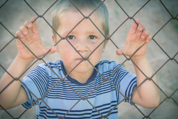 The child is behind bars. The boy is dirty, standing alone behind the cage.