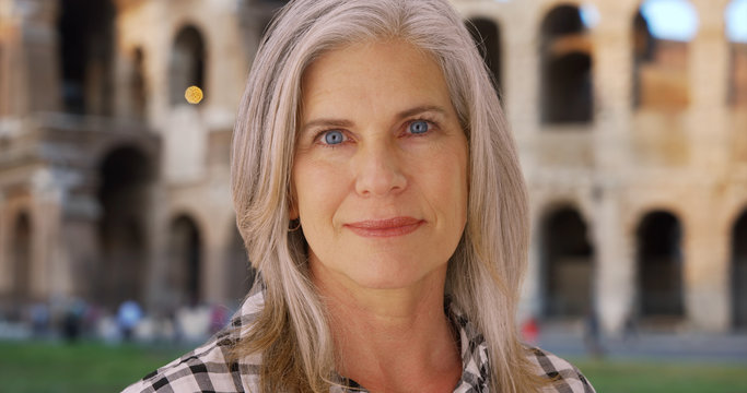 White female senior in front of the Colosseum in Rome looks intently at camera 