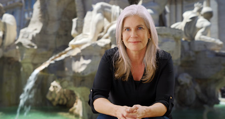 Happy woman in Rome sits and smiles in front of Fiumi Fountain