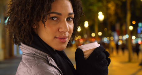 Gorgeous black female holds coffee cup smiling at camera on the Champs-Elysees