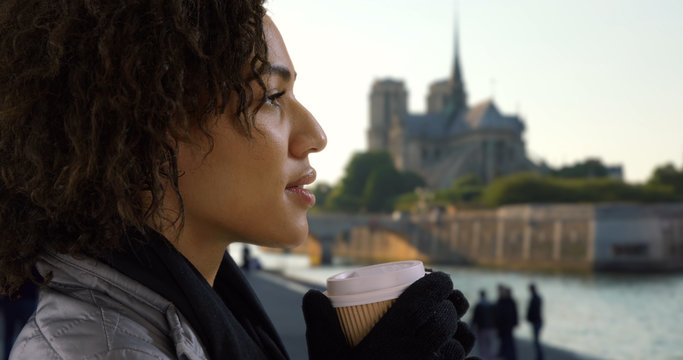 Close up of cute black female sipping coffee and looking around near Notre Dame
