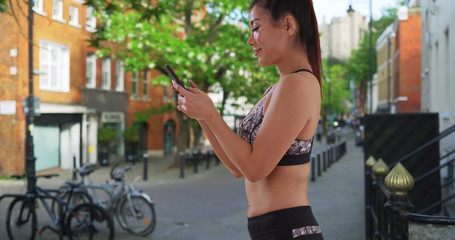 Happy attractive Asian female in running clothes texts on mobile phone