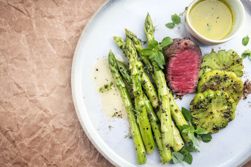 Modern barbecue dry aged sliced fillet steak with green asparagus and tomatoes as top view on a plate with copy space left