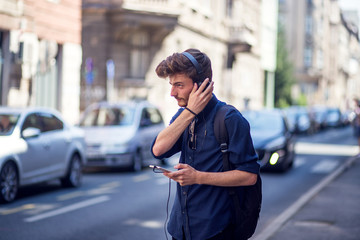 Fototapeta premium Portrait of handsome young man with cell phone and headphones listening to music on the street