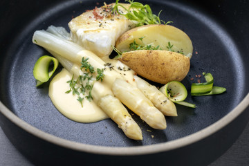 Modern German fried cod fish filet with white asparagus in hollandaise sauce und roast potatoes as...