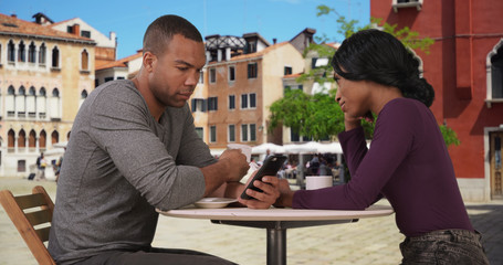 African-American man and woman check smartphones at cafe in Venice