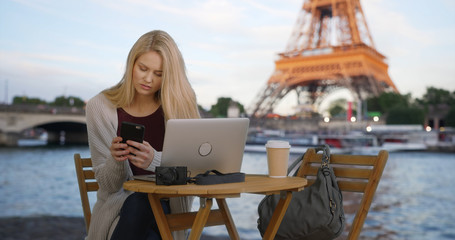 Young Caucasian female texts information from laptop near Eiffel Tower