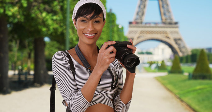Pretty African-American woman turns and takes photo of viewer near Eiffel Tower