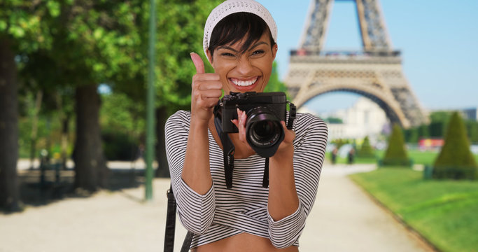 Pretty African-American woman turns and takes photo of viewer near Eiffel Tower