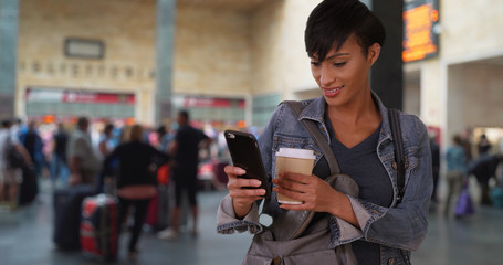 Young African female at train station lobby takes phone out to read text message