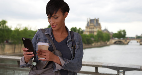 Obraz premium African-American beauty in Paris checking smartphone and drinking coffee