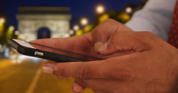 Close up of Latino professional male texting on cellphone near Arc de Triomphe