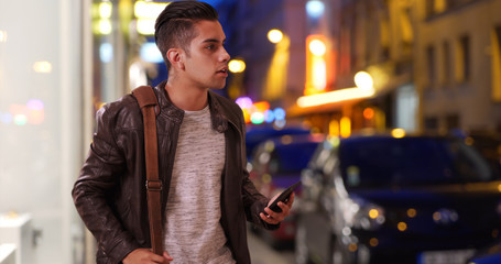 Latin millennial guy on city street at night hailing a cab or rideshare car