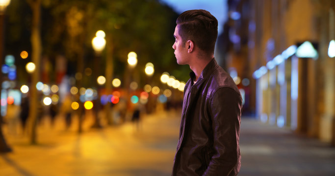 Hispanic millennial guy waiting for date on Champs-Elysees avenue at night