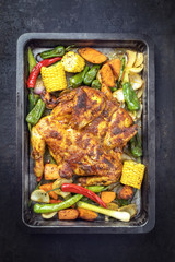 Spatchcocked barbecue chicken al mattone chili with corn and vegetable as top view on an old metal sheet