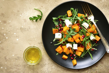 Delicious autumn pumpkin salad with arugula, feta cheese and pomegranate seeds.Top view with copy space.