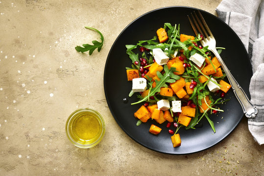 Delicious autumn pumpkin salad with arugula, feta cheese and pomegranate seeds.Top view with copy space.