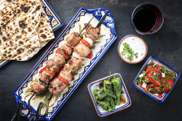 Traditional Greek souvlaki barbecue skewer with flatbread, tomato onion salad and tzatziki as top view on a plate