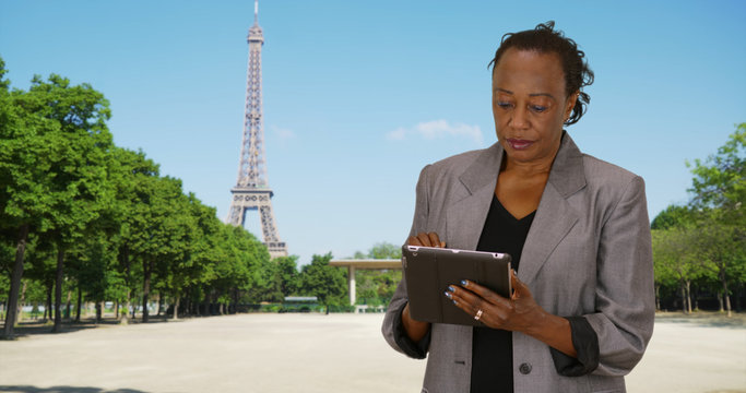 Happy mature woman uses digital tablet outdoors near Eiffel Tower
