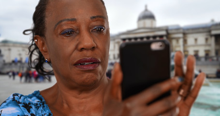 Black woman in Trafalgar Square looks at pictures of grandchildren on smartphone