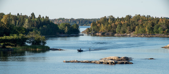 Summer vacation idyll in Sweden - A panorama view of Stockhol archipellago showing the sea, small islands and a motor boat towing a person on water skis.