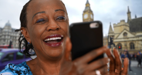 Black woman on London street looks at photos of grandkids on smartphone