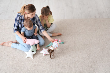 Mother with cute little children sitting on cozy carpet at home
