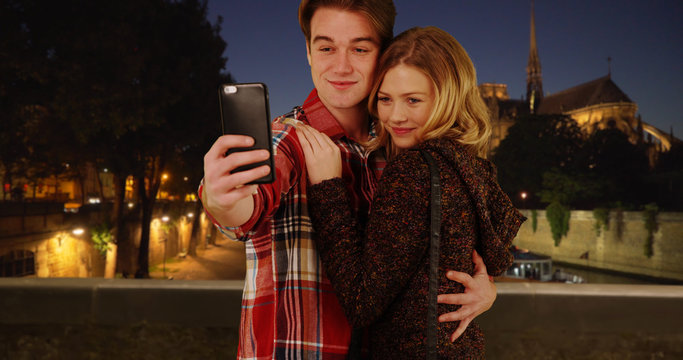 Happy young couple taking fun selfies in Paris at night