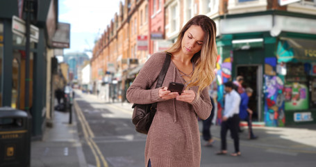 Naklejka na ściany i meble Young female walking through hipster neighborhood using cellphone