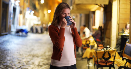 Casual portrait of woman drinking coffee outside restaurant at night