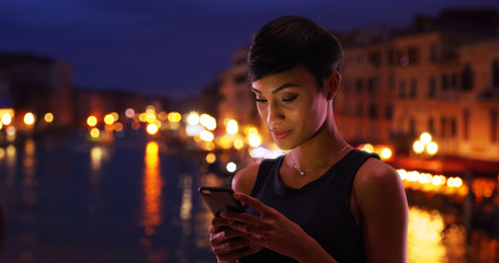 Pretty black woman traveling in Venice Italy reads her phone messages smiling