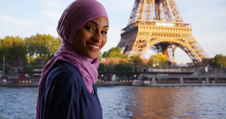 Happy beautiful young Muslim woman sightseeing by the Eiffel Tower and Seine