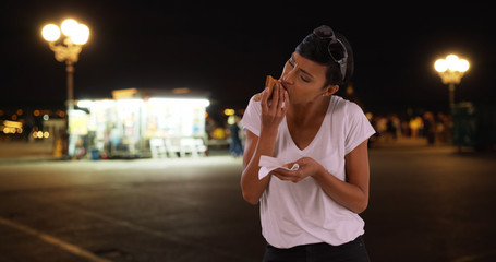 Young black woman enjoys slice of very cheesy pizza for dinner outside