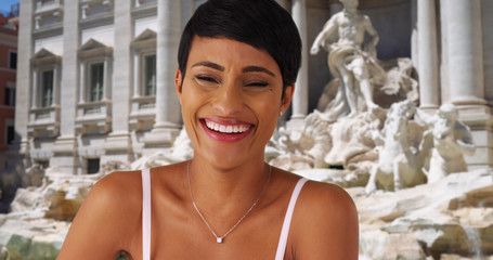 Pretty black woman sitting by the Trevi Fountain cannot contain her laughter