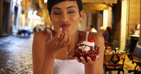 Black woman takes messy bite of huge red velvet cupcake